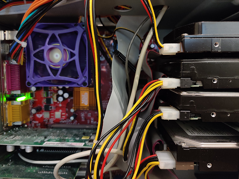 Et nostalgisk bilde av innsiden av en datamaskin. I forgrunnen sees fire harddisker, i bakgrunnen hovedkort med prosessor og vifte.